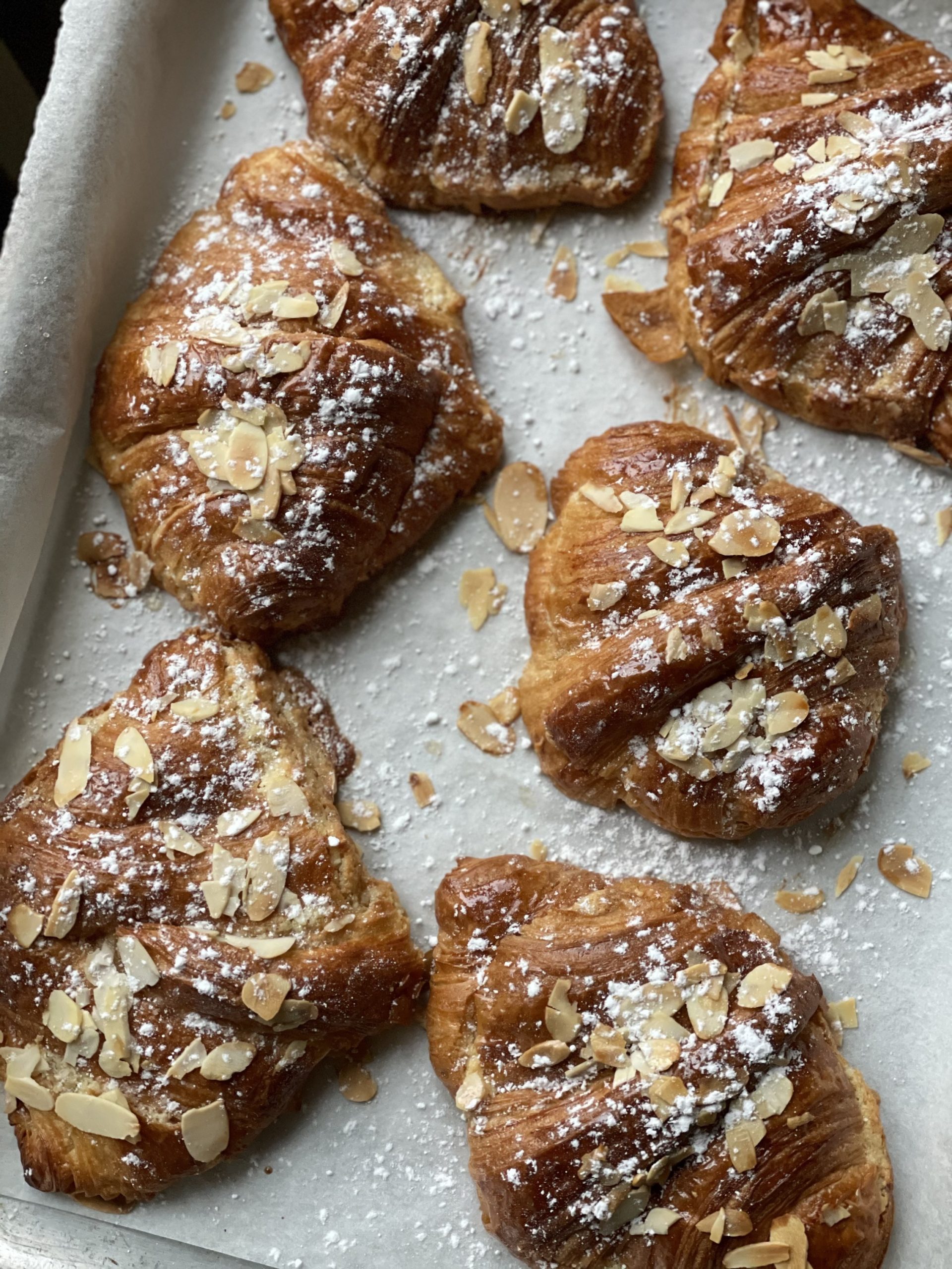 Freshly baked almond croissants topped with flaked almonds and icing sugarped with falkes