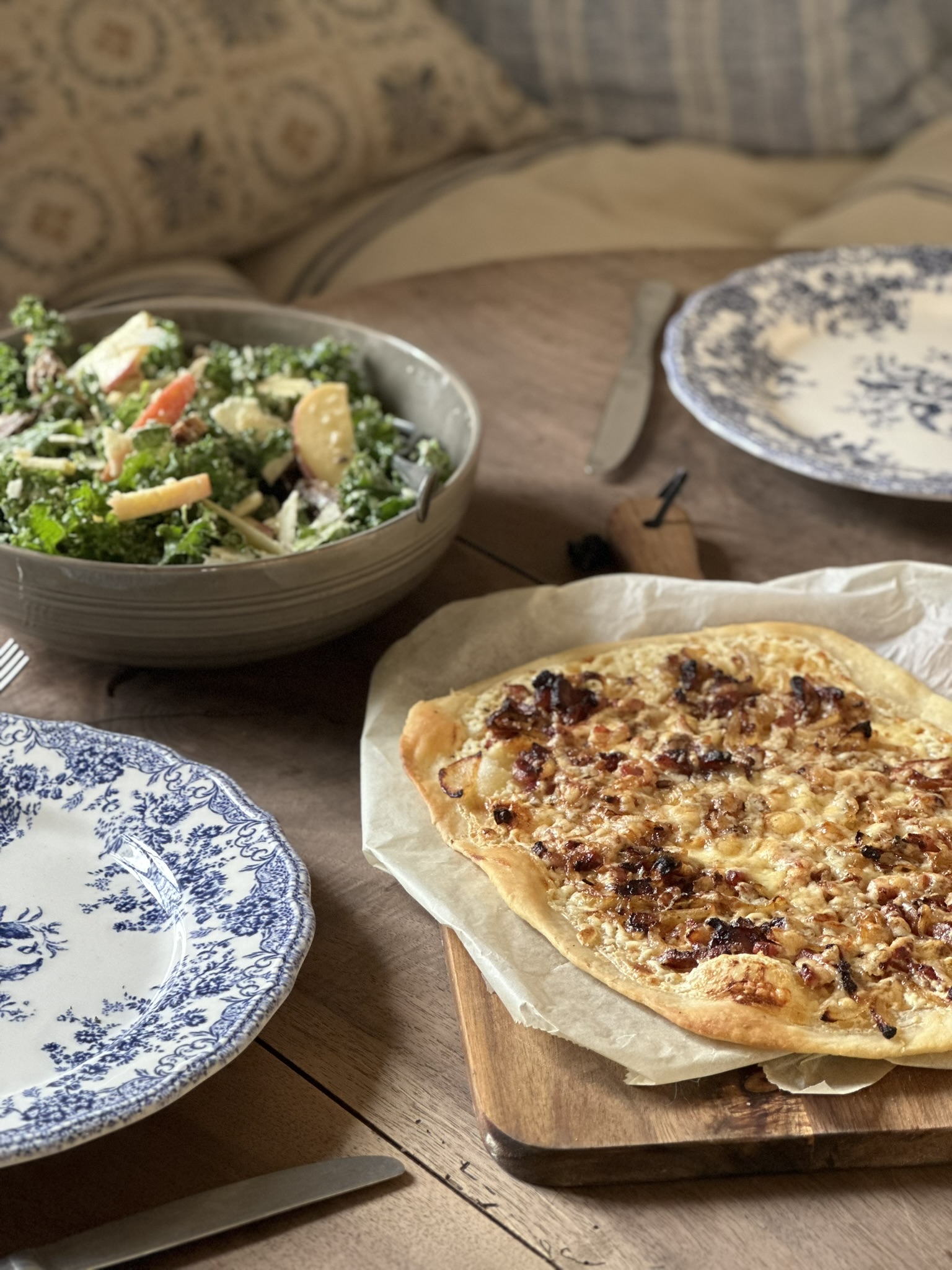 Tarte flambee a flat bread topped with seasoned creme fraiche, smokey bacon lardons and melted cheese, served on a table with a kale casear salad